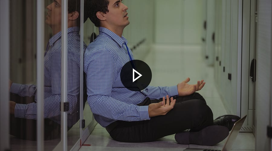 A dispairing IT technician sitting on the floor in a datacentre with his laptop